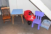 Wide view showing all five items: red Little Tikes car, wood rocker, small table, purple and blue plastic chairs.