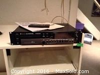 Tascam CD-RW900SL rackmount recorder on shelf with manual and remote on top