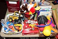 Overview photo showing assortment of vintage Tonka trucks, Hot Wheels cars in packaging, Spill & Spell and Yahtzee board games, various balls, children's books and stuffed toys.