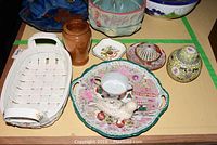 Photo showing a white woven basket, wood turned jar, various porcelain and ceramic items including a decorative plate, creamer, seal container, and small dishes.