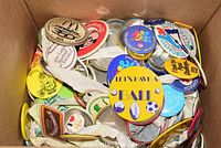 Top down view of a box containing assorted colorful vintage pinback buttons with various slogans and designs.