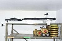 Weight bench with black padded seats and assorted weight plates and dumbbells on metal shelving