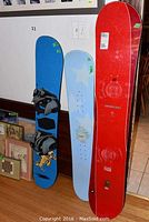 Three snowboards standing against a wall; red, blue with bindings, and light blue with star pattern visible.