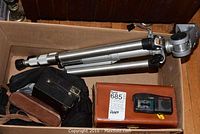 Box containing various vintage photography equipment including cameras, tripod, and recording device.
