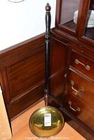Full view of the brass and copper bed warmer leaning against wooden furniture, showing the handle and warmer pan.