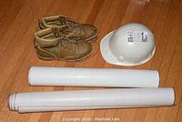 Photo showing the tan SECO size 8 boots, white Canadian-made hard hat, and three rolled tubs presumably containing posters or prints, laid on hardwood floor