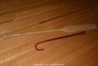 Wooden paddle oar and brown walking cane lying on wood floor, visible natural wood grain and minor wear.