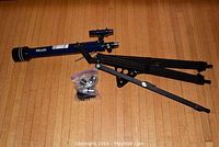 Blue Meade telescope with finder scope and black tripod on wooden floor, accompanied by plastic bag of accessories.