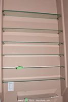 Seven mounted clear glass shelves on wall with metal support brackets, each shelf approximately 28 inches long and 5 inches deep.