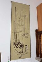 Full view of fabric wall hanging showing abstract boat design in black on beige fabric hung on a wall