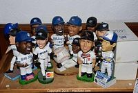 Overview of nine bobbleheads on shelf, showing Joe Carter, Cal Ripken, Pat Borders, Orlando Hudson glove display and two boxed figures