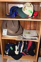 Top shelf and middle shelf showing multiple baseball caps including an Oakland Athletics cap and a blue 'S' cap, men's felt hats, and a stack of sports trading cards.