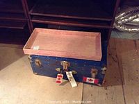 Blue metal trunk open with a wooden tray resting inside, showing the approximate interior space and wear on trunk surface.