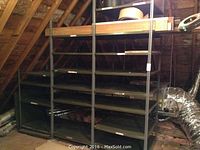 Wide view showing two large metal shelving units in an attic space with visible wooden rafters and ductwork. Shelves appear dark, with surface rust and wear.