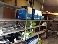 Side view of metal shelving unit loaded with boxes and some tools. Shelving is gray metal with adjustable holes and flat metal shelves.