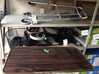 Two Nexus medical walkers with black mesh baskets and large wheels stacked on shelving alongside adjustable height bed tray with woodgrain laminated surface in storage.