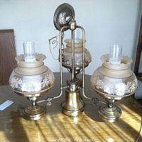 Front view of the brass tone three-branch ceiling light fixture showing the etched flower motif on flared glass shades with clear glass chimneys.