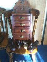 Wooden wall cabinet with four drawers sitting on a wooden chair with two carved wooden duck figures and two smaller bird carvings arranged in front of it