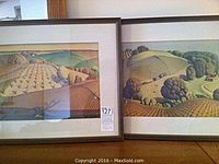 Photo showing two framed prints side by side, both with mats and dark frames, depicting stylized landscapes of farmland and hills.