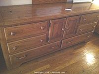 Full view of solid oak dresser with six drawers and central cabinet doors with wooden knob handles and metal handles on hidden drawers.