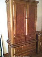 Front and side view of tall oak dresser with two doors closed, showing chevron wood panels and round wooden knobs.