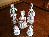 Wide view of all five Cordey porcelain Victorian figurines on a wooden table, showing two full-size figures and three busts.