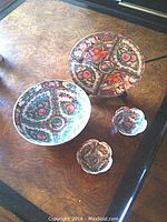 Four-piece lot shown on wood surface: one large floral painted bowl, one decorative figural plate, two small rice bowls with similar patterns.