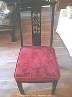 Full view of black lacquer wooden side chair with red velour seat cushion on wood flooring.