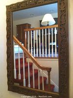Full view of the wall mirror showing the carved wooden leaf motif frame and reflective surface