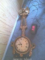Full view of gilt wood eagle clock with round dial, Roman numeral face, and decorative carved eagle on top, showing the clock is broken around the dial.