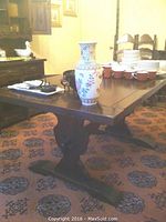 Full view of solid wood trestle dining table with decorative porcelain vase and tableware on top