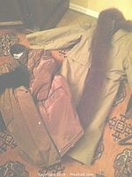 Two coats laid out side by side on a patterned carpet showing the light tan trench coat with fur trim and bronze satin coat with black fur collar.