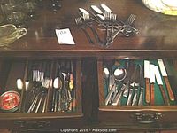 Top view showing two drawers and a surface with various knives, forks, and spoons, some with patterned handles.