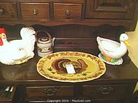 Photo showing ceramic turkey platter, white rooster soup tureen, and white duck bowl arranged on a wooden dresser
