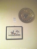 View showing one framed print of a mounted Californian Lancer soldier and one large round brass relief wall plate hung on the wall.
