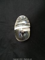 Top-down photo of clear glass sculpture paperweight showing white swirl inside and a bubble within the glass.