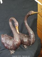 Two metal swan sculptures placed side by side showing full bodies and textured details on feathers with a dark finish and yellow painted beaks.