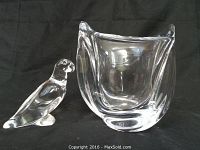 Baccarat lead crystal bird figurine beside leaded glass vase on black background.