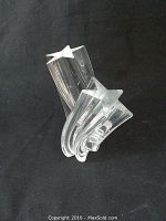 Front view of clear crystal sculpture with flowing curves and two star tips on a black background.