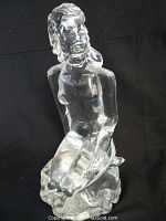 Full view of clear Murano glass female seated figure statue against black background.