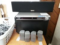Samsung silver front panel DVD player stacked with Cambridge Soundworks subwoofer and four Bose speakers in front, plus a laundry basket with cords to the left.