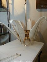 Chandelier laid on table with glass arms detached, showing eight white striped glass components and central gold frame.