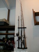 Four fishing rods with reels mounted vertically on a wall rack