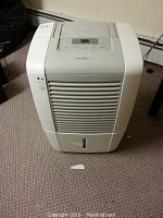 White Frigidaire dehumidifier with front air vent grille on carpeted floor.