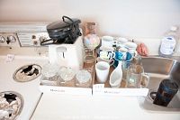 Small Proctor Silex waffle iron, two-slice toaster, three lidded glass jars, various cups, glasses and more shown on counter next to sink and stove.