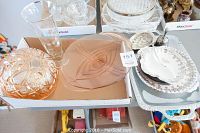 Photo of a box containing an amber tinted round bowl and large square serving plate, a tall etched glass vase, white china plates with floral rim stacked beside, and_clear glass dishes in background.