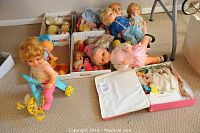 Photo showing a group of vintage dolls in two boxes and on the carpet, including a doll on yellow roller skates and multiple dolls with heavy wear.