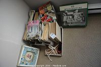 Overview photo showing stacks of vintage home decorating magazines, a boxed mini furniture planning kit, and a framed floral wall hanging on the floor.