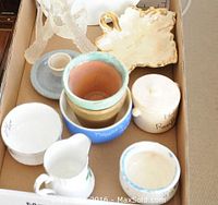 Multiple ceramic and porcelain vessels including Royal Stafford cream and sugar, small pitchers, and a leaf-shaped dish, all arranged in a cardboard box
