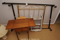 Photo showing brass colored metal headboard at the back with other wooden furniture items in front including flip-up table, plant stand, and shelf.
